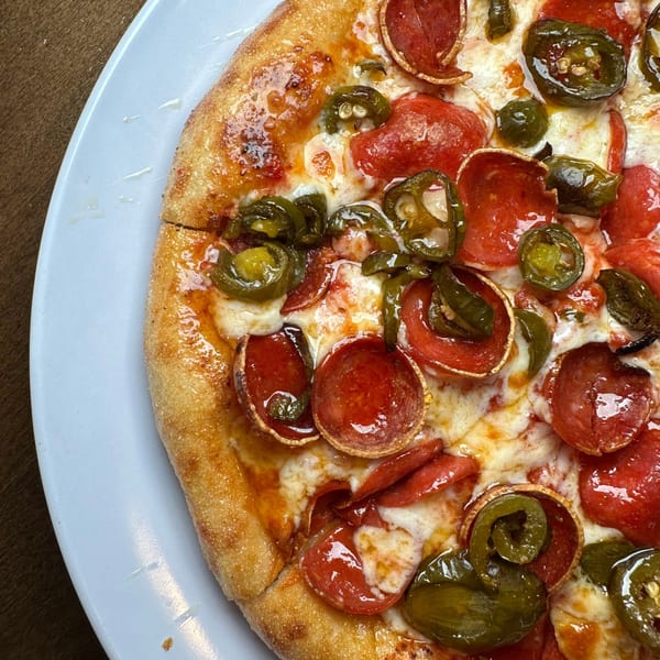 Close-up of a Pizza Buzz pepperoni and jalapeño pizza with melted cheese on a white plate.