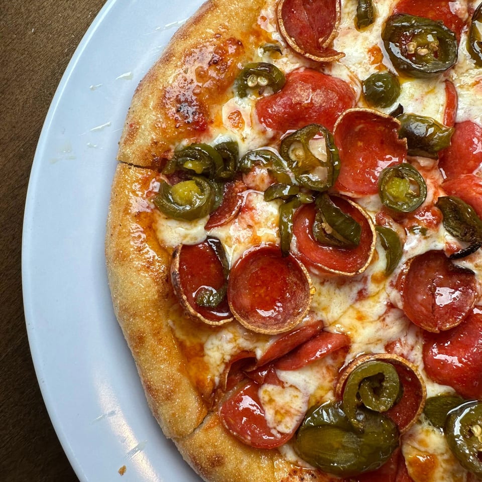 Close-up of a Pizza Buzz pepperoni and jalapeño pizza with melted cheese on a white plate.