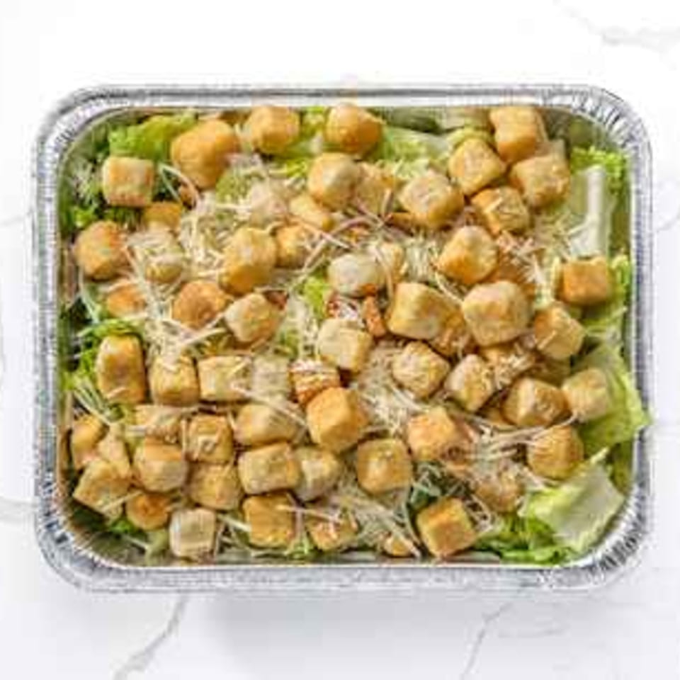 Caesar salad with croutons and shredded cheese in a foil take-out container.