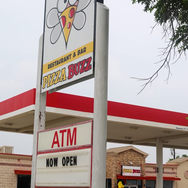 Pizza Buzz restaurant sign with a pizza slice logo, an ATM sign, and the building exterior.