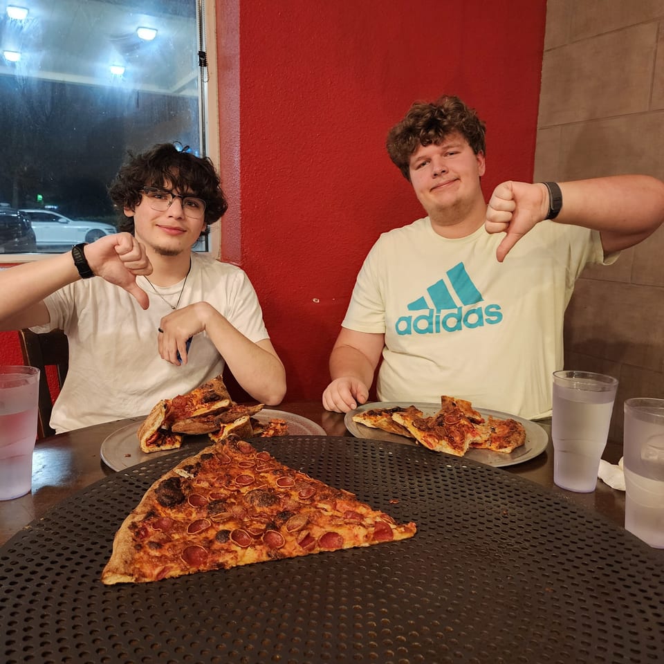 Two young men at Pizza Buzz give thumbs down to their pepperoni pizza slices.