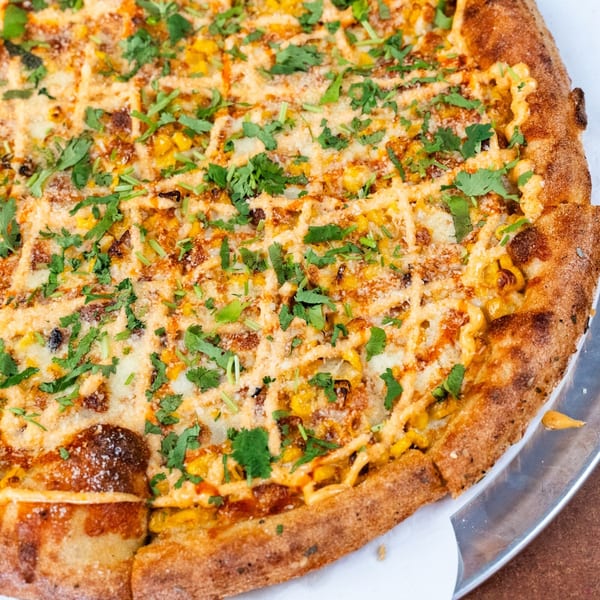 Close-up of a Pizza Buzz pizza topped with corn, cheese, a creamy sauce drizzle, and fresh cilantro.