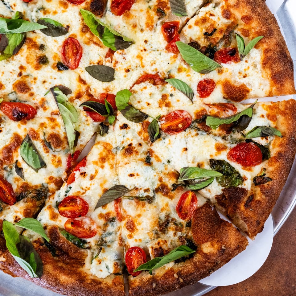 Close-up of a Pizza Buzz white pizza with roasted tomatoes, basil, and a crispy crust.