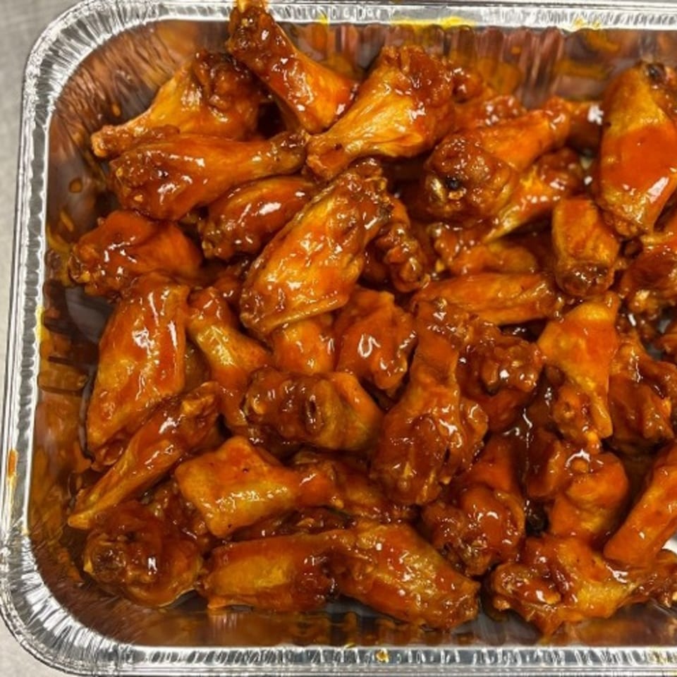 A foil tray filled with numerous glossy, orange-brown chicken wings, coated in a savory sauce.