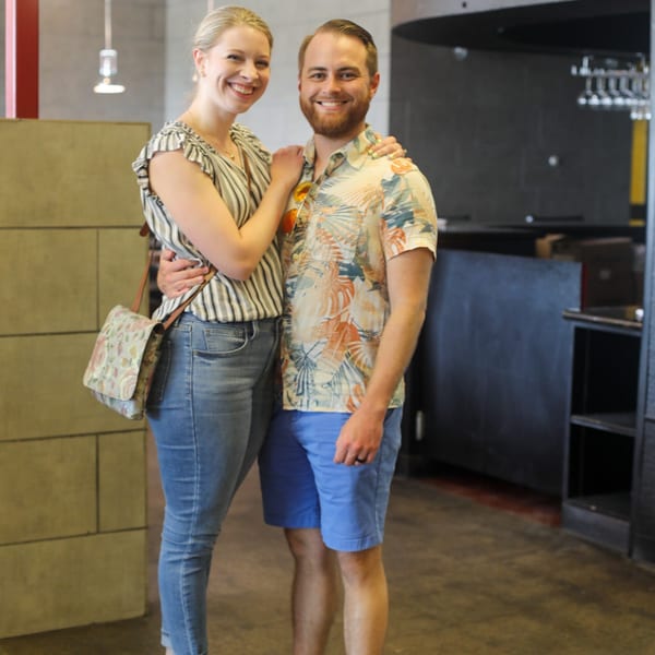 A smiling couple, a woman in a striped top and a man in a Hawaiian shirt, posing in a restaurant.