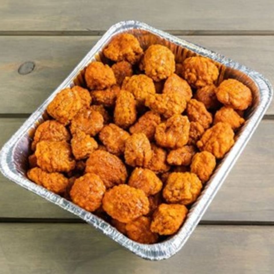 A foil tray filled with golden-brown, crispy boneless chicken wings from Pizza Buzz.