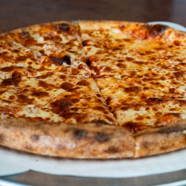 A close-up of a freshly baked Pizza Buzz cheese pizza, cut into slices, with a golden crust.