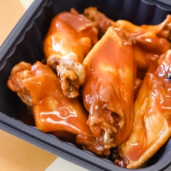 Close-up of several saucy chicken wings in a black takeout container from Pizza Buzz.