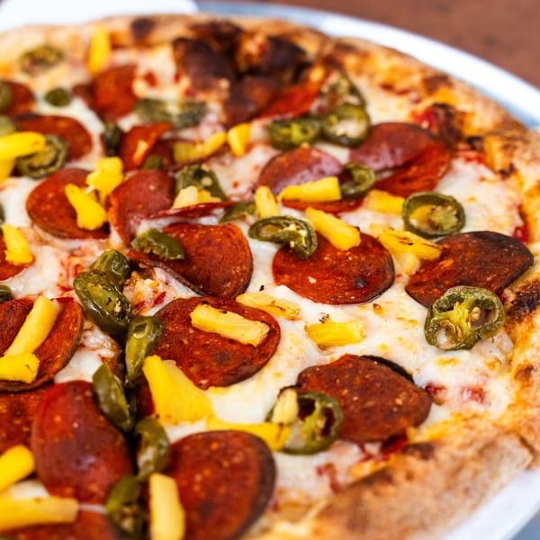 Close-up of a Pizza Buzz pizza with pepperoni, jalapeños, and pineapple on a white plate.
