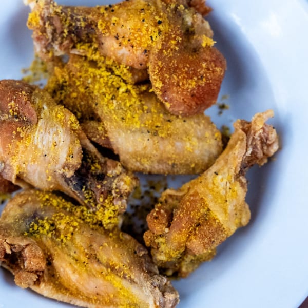 Close-up of crispy fried chicken wings generously dusted with yellow seasoning and black pepper on a light blue plate.