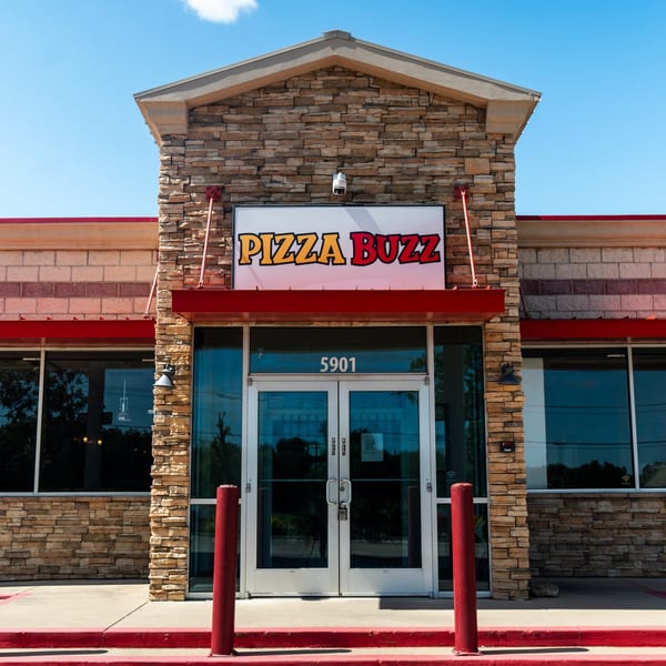 The exterior of Pizza Buzz, a stone-front building with a red awning and a prominent sign.