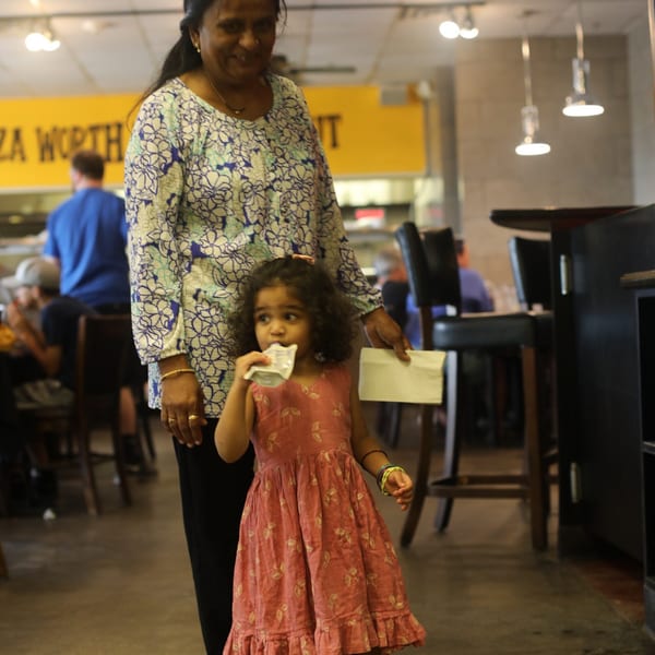 A woman and a young girl in a pink dress walk through the Pizza Buzz restaurant.